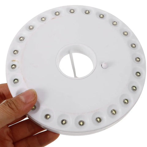 Hand holding LED Camping Lantern Round Waterproof Portable Tent Light for Hiking and Emergencies. Top view of white lamp.