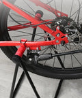 Close-up of a beefy heavy duty folding bike stand securing a red mountain bike, showing 360 degree clamp and aluminum frame for maintenance.