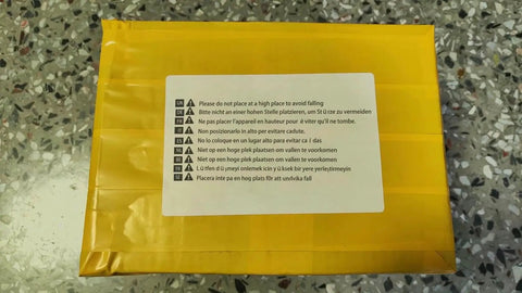 Yellow package with warning labels in multiple languages on a speckled surface, emphasizing safety instructions.