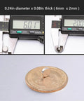 Close-up measuring of a 100 Pack Neodymium Disc Magnet 6mm x 2mm on a coin with a caliper for scale.