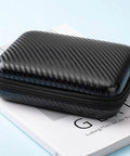 Rugged EVA External Hard Drive Case Pouch For SSDs And HDDs resting on a book, black carbon fiber texture.