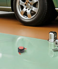 Badass Two Pack Aerosol Self Activating Auto Fire Extinguisher Sticker With Sticky Adhesive Backing For Car Engine Garage Or Rig That Takes Care Of Smoke Quick on a garage floor next to a car wheel.