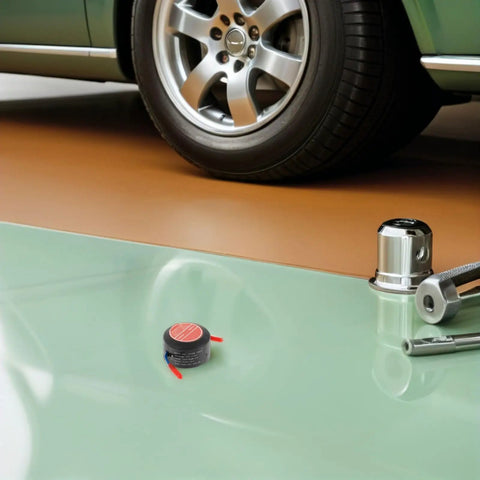 Badass Two Pack Aerosol Self Activating Auto Fire Extinguisher Sticker With Sticky Adhesive Backing For Car Engine Garage Or Rig That Takes Care Of Smoke Quick on a garage floor next to a car wheel.