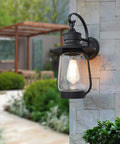 Rock Solid Outdoor Wall Lantern With Slick Industrial Design And Transparent Bubble Glass Shade Featuring A Top Shelf Led Filament Bulb For Sweet Porch Lighting And Dreamy Patio Vibes In Heavy Duty Black Coating mounted on a stone wall.