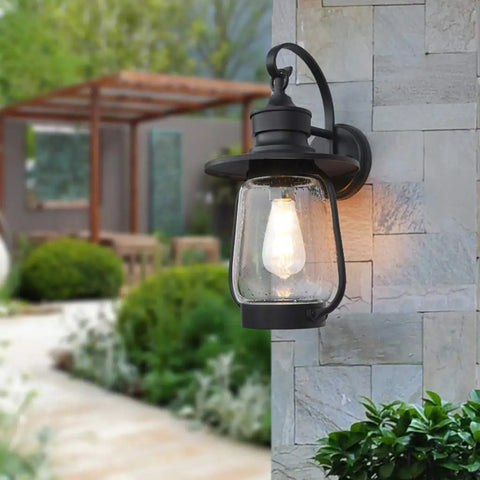 Rock Solid Outdoor Wall Lantern With Slick Industrial Design And Transparent Bubble Glass Shade Featuring A Top Shelf Led Filament Bulb For Sweet Porch Lighting And Dreamy Patio Vibes In Heavy Duty Black Coating mounted on a stone wall.