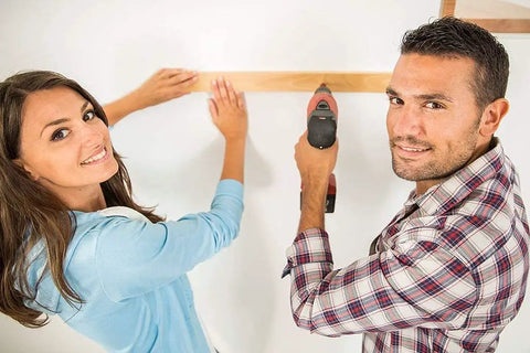 Two people using a drill to install a wooden beam on a wall.