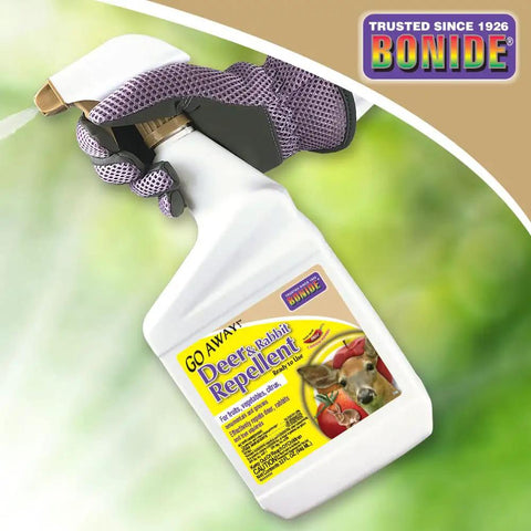 Hand holding Go Away Deer And Rabbit Repellent Spray 32 Oz Ready To Use Hot Pepper Formula bottle against green background.