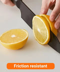 Person slicing a lemon with a black friction resistant knife on a white cutting board.