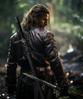 Warrior wearing Medieval Leather Back Sword Shoulder Frog With Adjustable Sheath Holster, standing in forest, sword visible on back.