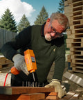 Man using Pro Grade Air Punch Nailer Nail Remover Pneumatic Puller For Denailing And Wood Recycling on wooden pallets outdoors