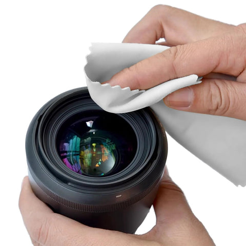 White microfiber cleaning cloth used to wipe a camera lens; close-up of hands holding the cloth.