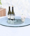 Top Shelf Tempered Glass Lazy Susan Turntable With Zero Friction Bearing Spin Smooth Glide Rotating Serving Tray For Kitchen Island Party Banquet Round Design on table with wine bottles, glasses, and flowers.