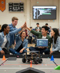 Students celebrating successful Raspberry Pi Mecanum Robot Kit project with laptop and robot on competition floor.