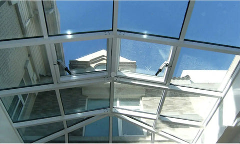 View of a glass skylight with white framing, showcasing the bright blue sky above a building.