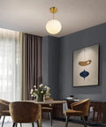 Globe Pendant Light With Matte White Milk Glass And Brass Finish in dining room setting, modern one light fixture with swivel canopy.