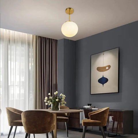 Globe Pendant Light With Matte White Milk Glass And Brass Finish in dining room setting, modern one light fixture with swivel canopy.