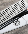 Slick Steel Shower Drain Hook With Soft Silicone Grips And Easy Pull Strip Feature For Hassle Free Drain Cover Removal Plus Linear Grate Extraction In No Sweat Bathroom Set Gray being used to lift a drain grate.
