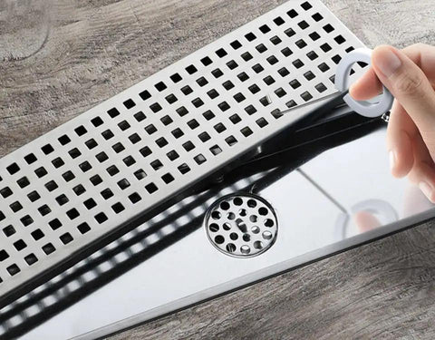 Slick Steel Shower Drain Hook With Soft Silicone Grips And Easy Pull Strip Feature For Hassle Free Drain Cover Removal Plus Linear Grate Extraction In No Sweat Bathroom Set Gray being used to lift a drain grate.