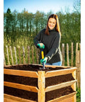 Person using Compact 30 Inch Mini Shovel for Precision Digging in a raised garden bed, fiberglass handle visible.