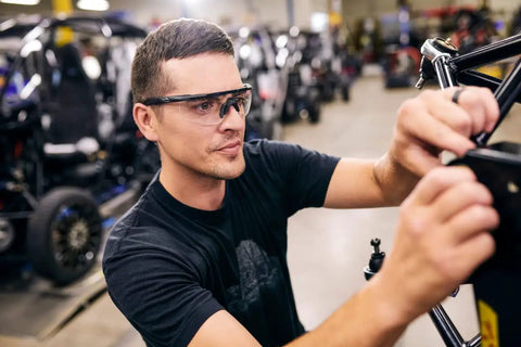 Badass Tactical Shooting Safety Glasses With Interchangeable Lenses, matte black frame worn by a man working in a workshop.