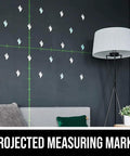 Self Leveling Green Cross Line Laser With Projected Measuring Marks For Quick Precise Layouts Up To 65 Feet A Handy DIY And Pro Tool Red Black LL932401 showing projected green lines with measuring marks on a wall above a couch and floor lamp.