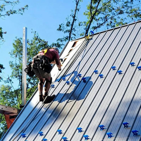 Worker using heavy-duty roof safety anchor on steep metal roof for first man up and last man down, 5,000-lb capacity.