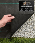 Hand showing Heavy Duty Weed Barrier Fabric 4 Ft By 50 Ft Durable Woven Ground Cover, layered over gravel and grass, partially lifted.