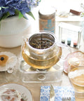 Kyoto 2-In-1 Tea Kettle And Tea Maker Glass Teapot with loose-leaf infuser on table setup with tea cups and floral decorations