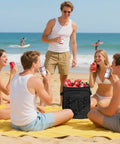 Friends enjoying a beach picnic with a Beast 40 Can Insulated Cooler Backpack With Dual Leak Proof Compartments in black.