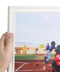 Hand holding Fresh White Wooden Photo Frame 8X12 Inch Ready To Hang Clean Wall Decor With Crystal Clear Glass featuring a baseball scene.