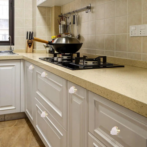 Four Crisp White Geode Cabinet Knobs With Burnished Gold Plating on white kitchen drawers enhancing modern decor.