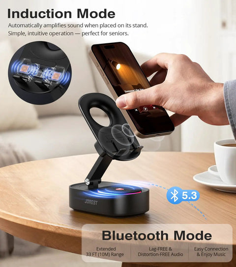 Person placing smartphone on foldable Wireless Induction Speaker Phone Stand With Bluetooth Audio Amplifier, on a table.
