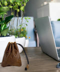 Hardy Cowhide Leather Drawstring Pouch With Vintage Retro Finish Designed For Hauling Your Daily Grind Essentials Travel Toiletries And Quick Pocket Stash next to a laptop on a table.
