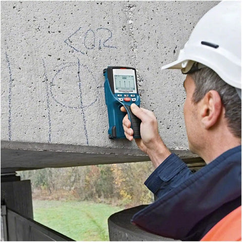 A contractor using a wall scanner on concrete to locate hidden objects, featured in Nail Your Next Home Project Straight Up With This Hella Reliable Wall Scanner And Metal Detector Featuring Millimeter Exact Center Targeting For Busy Contractors.