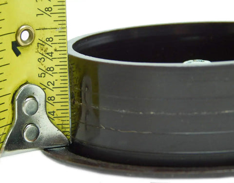 Close-up of a brown desk grommet with a measuring tape showing its 2-3/8 inch diameter for cable organization use.