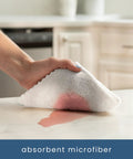White microfiber cleaning cloth held in hand wiping a kitchen countertop; 11.8 x 11.8 inches