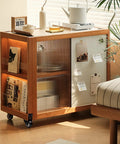 Wooden storage cabinet on wheels next to a bed with books, decorative items, and glass sliding door in a sunlit room.