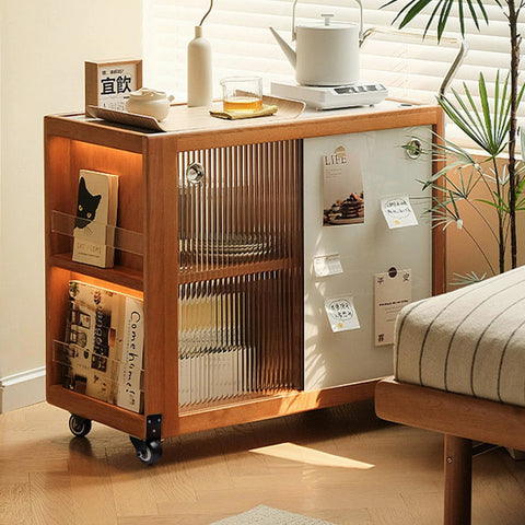 Wooden storage cabinet on wheels next to a bed with books, decorative items, and glass sliding door in a sunlit room.