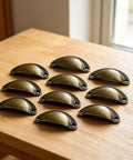10 Piece Set Of Badass Antique Bronze Cup Pull Handles With Classic Half Moon Shell Design, Heavy Duty Solid Iron Hardware For Dresser And Closet on wooden surface.