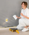 Woman holding a two pack adhesive spreader trowel with three sixteenth inch notch for epoxy projects next to a painted wall.