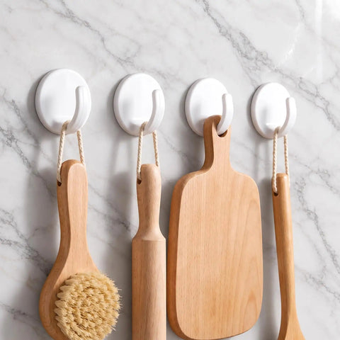 Eight Piece White Peel And Stick Wall Hooks Offer A Super Strong Hold that organizes wooden kitchen utensils on a marble wall.