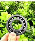 Top Tier Silicon Nitride Full Ceramic Ball Bearing 6210CEF Sized At 50X80X20mm shown against greenery.