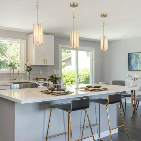 Elegant gold pendant lighting with white glass cylinder illuminates modern kitchen island with dining setup.