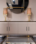 Modern sideboard with matte black cabinet handles, adorned with two gold lamps, reflecting in a round mirror above.