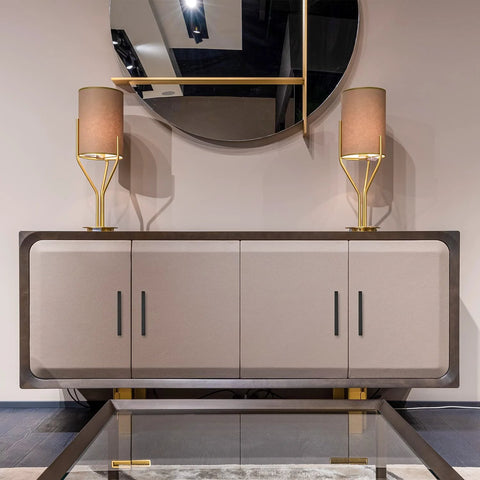 Modern sideboard with matte black cabinet handles, adorned with two gold lamps, reflecting in a round mirror above.