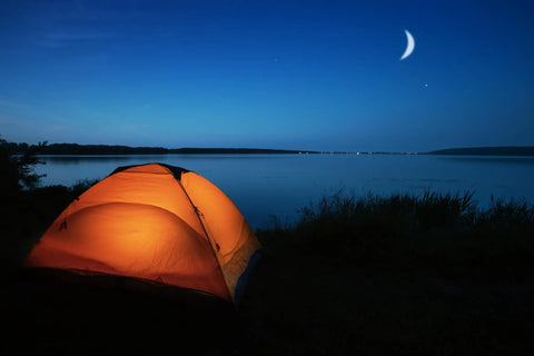 Illuminated tent by a lakeside under crescent moon, perfect setting for using a 2-Cell CR123 LED Tactical Flashlight With High-Brightness Beam