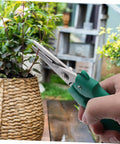 Hand holding stainless steel pruning scissors garden shears for branch cutting easy to use gardening tool near plant