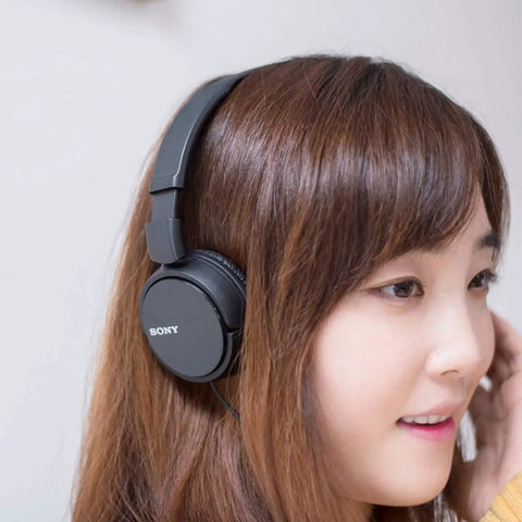 Go Anywhere Plug And Play Wired On Ear Headphones With Snug Foam Tips And Sturdy Swivel Cups Built For Long Commutes And Chill Vibes In Classic Black worn by a woman.