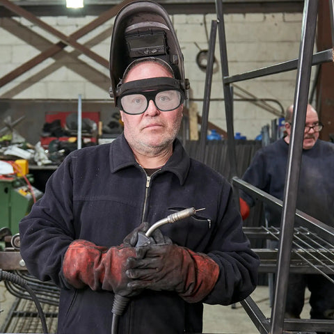 Heavy Duty Flip Up Auto Darkening Welding Goggles Rock Solid Impact Resistant Safety Glasses worn by a welder in a workshop.