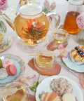 Stovetop And Microwave Safe Glass Teapot With Removable Infuser on a table with blooming teas and pastries, 34 oz borosilicate glass